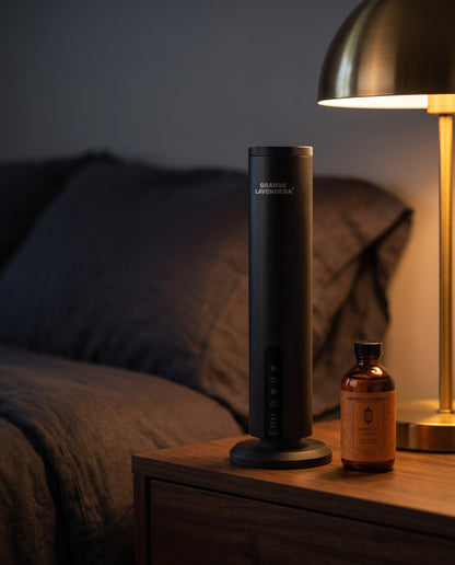 Grande Lavendera Smart App Waterless Aroma Diffuser with 4 oz Moroccan Amber diffuser oil on a nightstand at night, introductory offer set